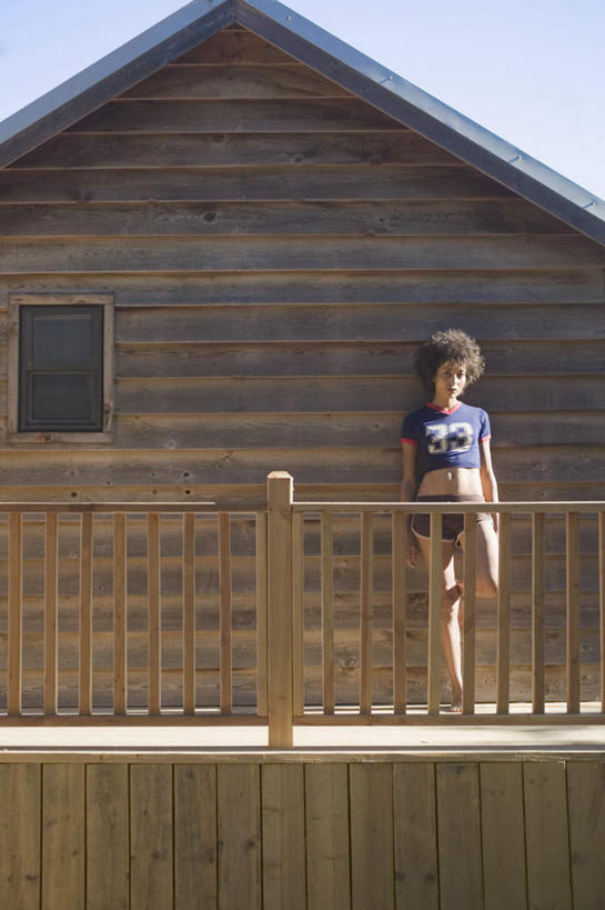 西方人,一个人,木屋,栏杆,站,笑,微笑,竖图,室外,白天,正面,旅游,度假,建筑,欧洲,非洲,黑人,欧洲人,仅一个人,服装,木制,房屋,围栏,抬腿,注视,休闲装,娱乐,衣服,扶,观察,看,靠,靠着,站着,享受,休闲,休闲服,放松,抬脚,服饰,观看,单脚,察看,扶着,关注,年轻女性,女人,女性,非洲人,卷发,站立,彩图,全身,房子,木杆