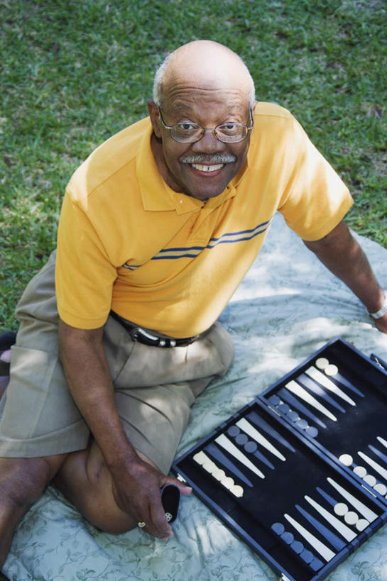 西方人,一个人,坐,笑,微笑,露齿笑,竖图,俯视,室外,白天,游戏,快乐,赌博,贪欲,比赛,竞争,草地,草坪,植物,欧洲,非洲,黑人,欧洲人,仅一个男性,仅一个人,服装,坐垫,玩,注视,休闲装,娱乐,刺激,草,衣服,黄色,绿色,观察,看,仅一个老年男性,休闲,休闲服,棋盘,服饰,观看,活动,察看,发泄,关注,消遣,智力,双陆棋,投机,侥幸,欲望,宣泄,野餐垫,野餐地毯,多功能毯,双陆,老年男性,男人,男性,非洲人,抬头,玩耍,嬉戏,仰头,坐着,半身,彩图,高角度拍摄,胜负,输赢