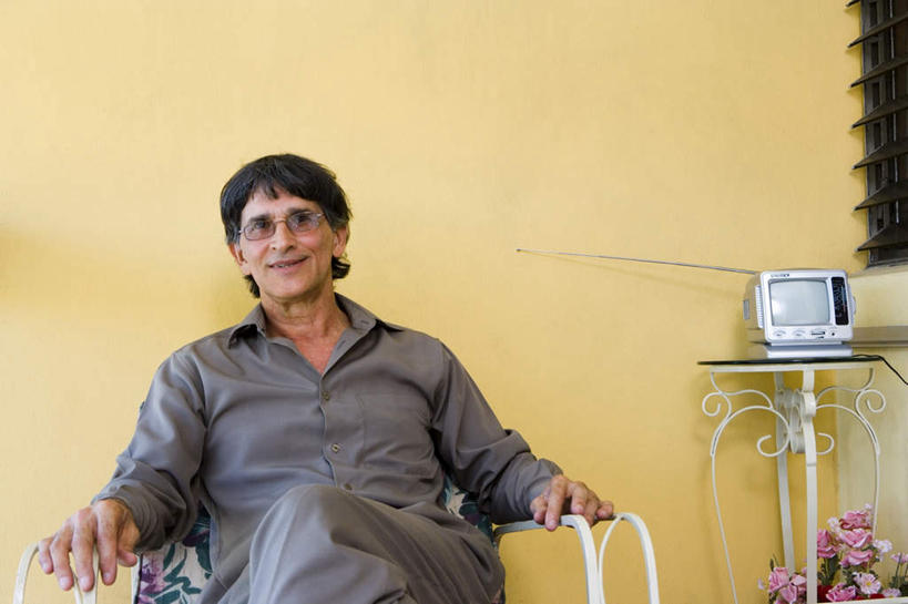 西方人,一个人,坐,笑,微笑,露齿笑,横图,室内,白天,正面,窗户,桌子,电视,椅子,欧洲,欧洲人,仅一个男性,仅一个人,盛开,百叶窗,墙,花蕾,注视,墙壁,墙面,花,花瓣,花朵,鲜花,黄色,花苞,花蕊,观察,看,仅一个老年男性,观看,察看,关注,彩电,彩色电视机,显像管屏,显像管屏幕,老年男性,男人,男性,白种人,电视机,坐着,半身,彩图